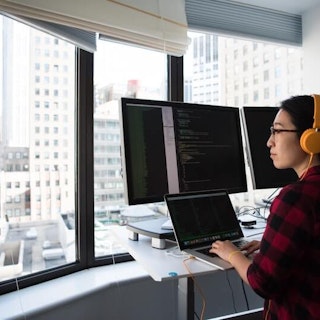 A student wearing headphones sits in front of multiple computer screen monitors.